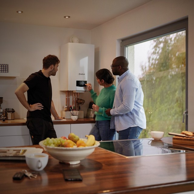  three people standing around the boiler in the kitchen