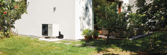 aroTHERM heat pump on the side of a white wall with grass in front
