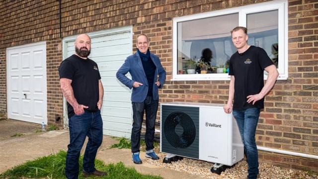 three installers, one being Kevin McCloud standing around a heat pump