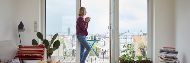 woman holding a cup of tea standing looking out a large window in a flat