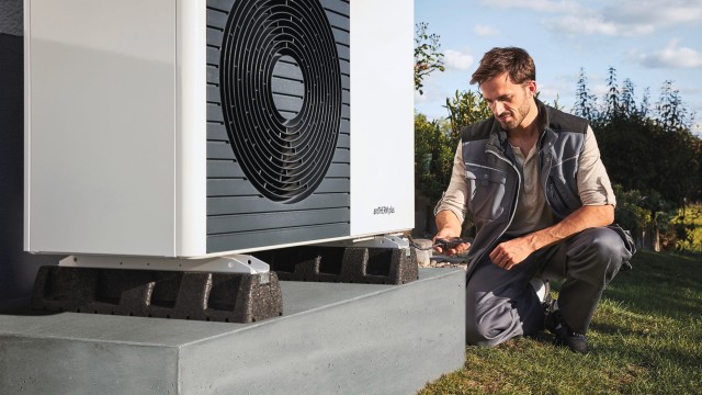 installer carrying out work on a heat pump. He is kneeling on the ground holding a device looking down