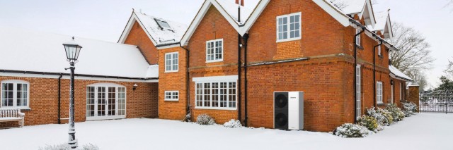 A red brick house surrounded by a blanket of snow on the ground, creating a picturesque winter scene.