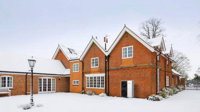 A red brick house surrounded by a blanket of snow on the ground, creating a picturesque winter scene.