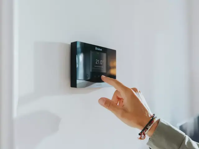 a senso heating control on a white wall with a hand touching the thermostat.